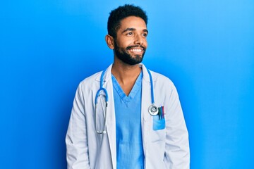Handsome hispanic man with beard wearing doctor uniform and stethoscope looking to side, relax...