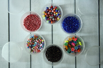 Multicolored beads in round plastic boxes on a wooden background.