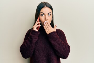 Young brunette woman having conversation talking on the smartphone covering mouth with hand,...