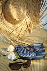 A group of beach objects, shells, sunglasses, straw hat, flip-flop sandal.