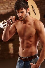 Sexy latin lover holding guitar with bare upper body.