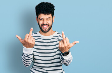 Young arab man with beard wearing casual striped sweater showing middle finger doing fuck you bad...