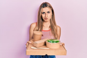 Beautiful hispanic woman holding tray with healthy lunch skeptic and nervous, frowning upset...