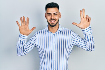 Fototapeta premium Young hispanic man with beard wearing casual striped shirt showing and pointing up with fingers number eight while smiling confident and happy.