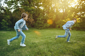 Two brother boys running outdoors in park at sunset time. High quality photo