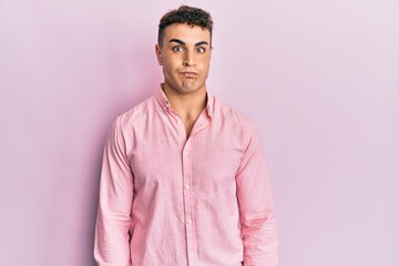 Hispanic young man wearing casual clothes puffing cheeks with funny face. mouth inflated with air,...