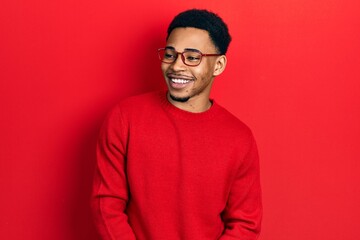 Young african american man wearing casual clothes and glasses looking away to side with smile on face, natural expression. laughing confident.