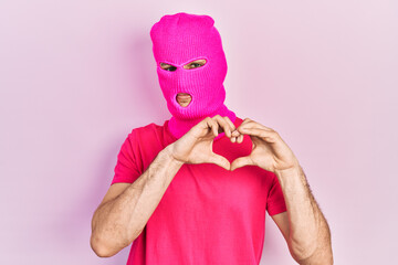 Young hispanic man with modern dyed hair wearing pink balaclava mask face smiling in love doing...