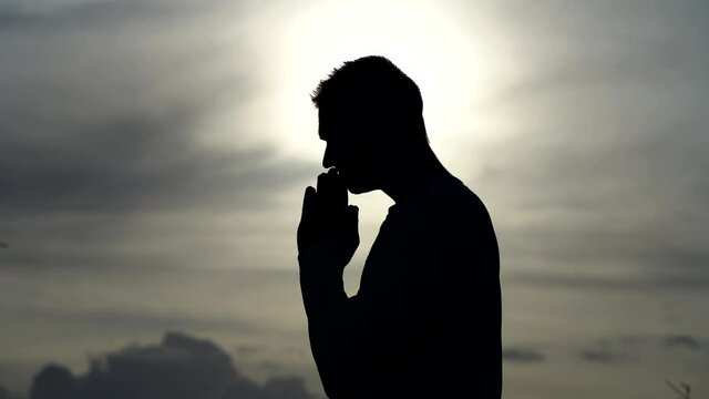 Silhouette of Man pray on during sunset. Religion, faith and hope concept 
