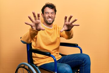 Handsome man with beard sitting on wheelchair smiling funny doing claw gesture as cat, aggressive and sexy expression