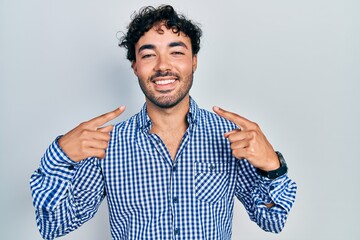 Young hispanic man wearing casual clothes smiling cheerful showing and pointing with fingers teeth and mouth. dental health concept.