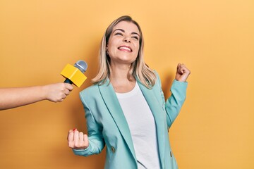 Beautiful caucasian woman being interviewed by reporter holding microphone very happy and excited...