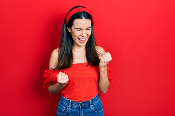 Obraz na płótnie Canvas Young brunette woman wearing casual red shirt celebrating surprised and amazed for success with arms raised and eyes closed