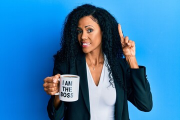 Middle age african american woman drinking from i am the boss coffee cup smiling with an idea or...