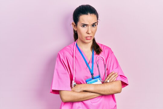 Young brunette woman wearing doctor uniform and stethoscope standing with arms crossed clueless and confused expression. doubt concept.