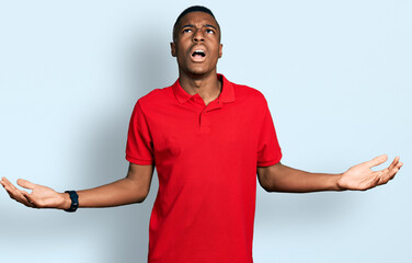 Young african american man wearing casual red t shirt crazy and mad shouting and yelling with...