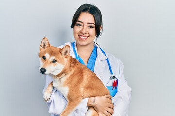 Beautiful hispanic veterinarian woman holding dog smiling with a happy and cool smile on face. showing teeth. - obrazy, fototapety, plakaty
