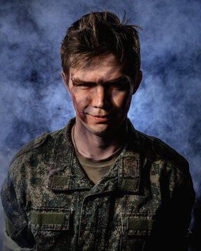 Portrait of a close-up of a soldier in scars and battle paint against the background of smoke