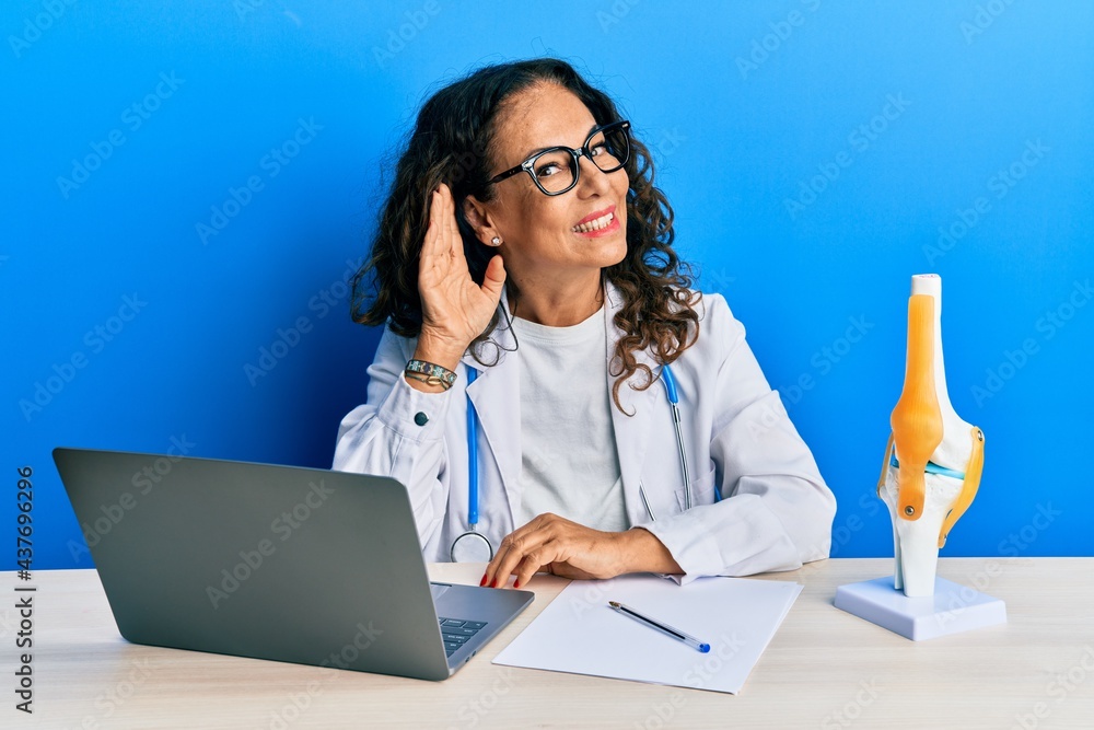 Sticker beautiful middle age woman doctor at orthopedic clinic smiling with hand over ear listening an heari