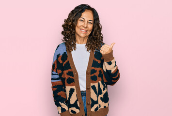 Middle age hispanic woman wearing casual clothes smiling with happy face looking and pointing to the side with thumb up.