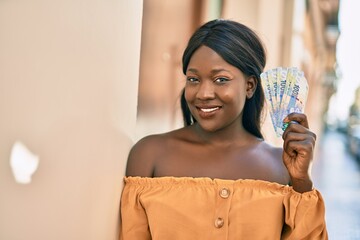 Young african american woman smiling happy holding south africa rands at the city.