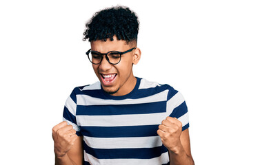 Young african american man wearing casual clothes and glasses very happy and excited doing winner gesture with arms raised, smiling and screaming for success. celebration concept.