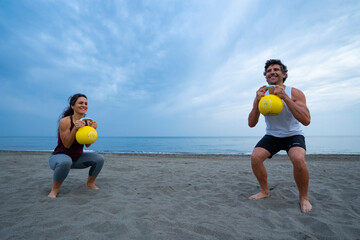couple of athletes exercising on the beach with kettle bells