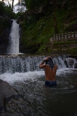 a young asian man bathing in a fresh waterfall on a sunny day