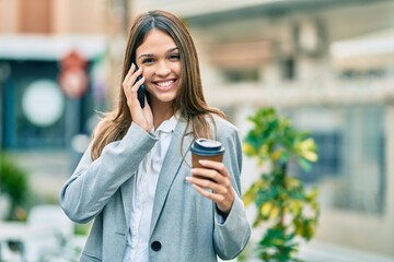 Young latin businesswoman talking on the smartphone drinking coffee at the city.