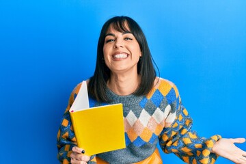 Obraz premium Young hispanic woman reading book celebrating victory with happy smile and winner expression with raised hands