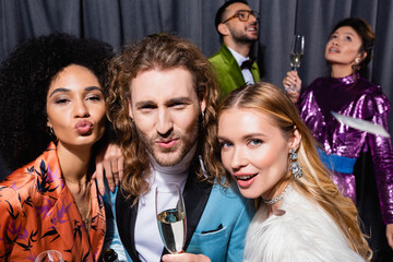 happy interracial friends in stylish clothes drinking champagne on grey background.