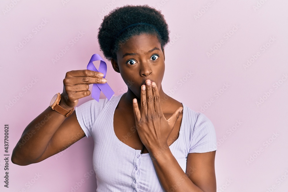 Wall mural Young african american girl holding purple ribbon awareness covering mouth with hand, shocked and afraid for mistake. surprised expression