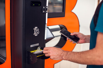 Bitcoin ATM. Man using bitcoin atm to buy or to sell crypto coins.