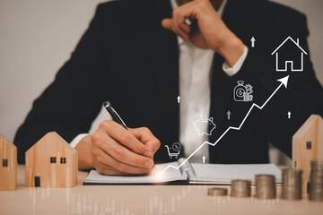 Businessman hand write in book note and icon business graphs with mini wood house model from model on wood table, Planning buy Real Estate, Planning to buy property. concept of Choose the best.