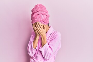 Young man wearing woman make up wearing shower towel on head and bathrobe with sad expression covering face with hands while crying. depression concept.