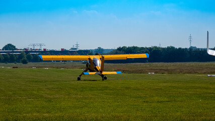 R&uuml;ckansicht eines blau gelben Propellerflugzeug beim Startvorgang auf einer Natur Startbahn