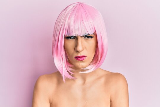 Young man wearing woman make up wearing pink wig skeptic and nervous, disapproving expression on face with crossed arms. negative person.