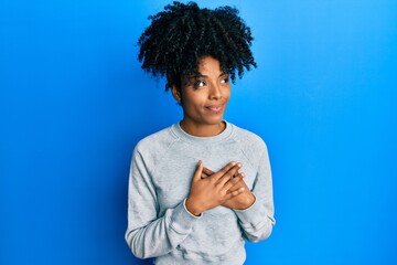 African american woman with afro hair wearing sportswear doing heart symbol with hands smiling looking to the side and staring away thinking.