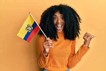 African american woman with afro hair holding ecuador flag pointing thumb up to the side smiling happy with open mouth
