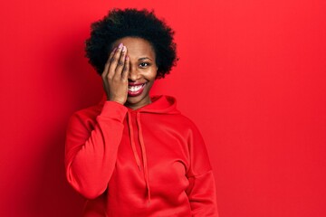 Fototapeta na wymiar Young african american woman wearing casual sweatshirt covering one eye with hand, confident smile on face and surprise emotion.