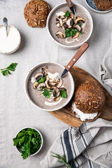 Traditional French mushroom cream soup with sour cream and parsley and rye bun on wooden board on natural linen background .
