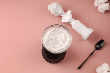 Health and beauty concept. Hydrolyzed collagen in a glass cup and black spoon on a pink background. Natural anti-aging supplement for beauty spa treatments. Copy space