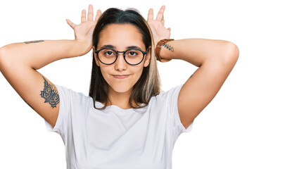 Young hispanic woman wearing casual white t shirt doing bunny ears gesture with hands palms looking cynical and skeptical. easter rabbit concept.