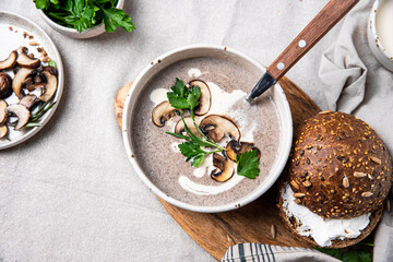 Traditional French mushroom cream soup with sour cream and parsley and rye bun on wooden board on natural linen background .