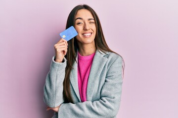 Young hispanic girl holding credit card winking looking at the camera with sexy expression,...