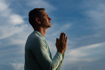 Young Man pray on blue sky background. Religion, faith and hope concept  - obrazy, fototapety, plakaty