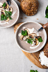 Traditional French mushroom cream soup with sour cream and parsley and rye bun on wooden board on natural linen background .