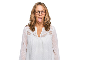 Middle age blonde woman wearing casual white shirt and glasses sticking tongue out happy with funny expression. emotion concept.