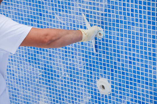 Pool renovation work. A worker lays the tiles and covers the seams in the pool