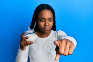African american woman with braided hair holding bowl of sugar candy pointing with finger to the camera and to you, confident gesture looking serious
